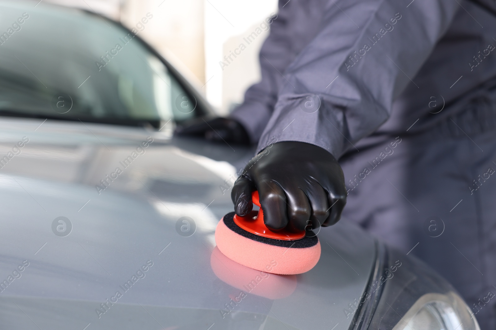 Photo of Man polishing car hood with sponge indoors, closeup