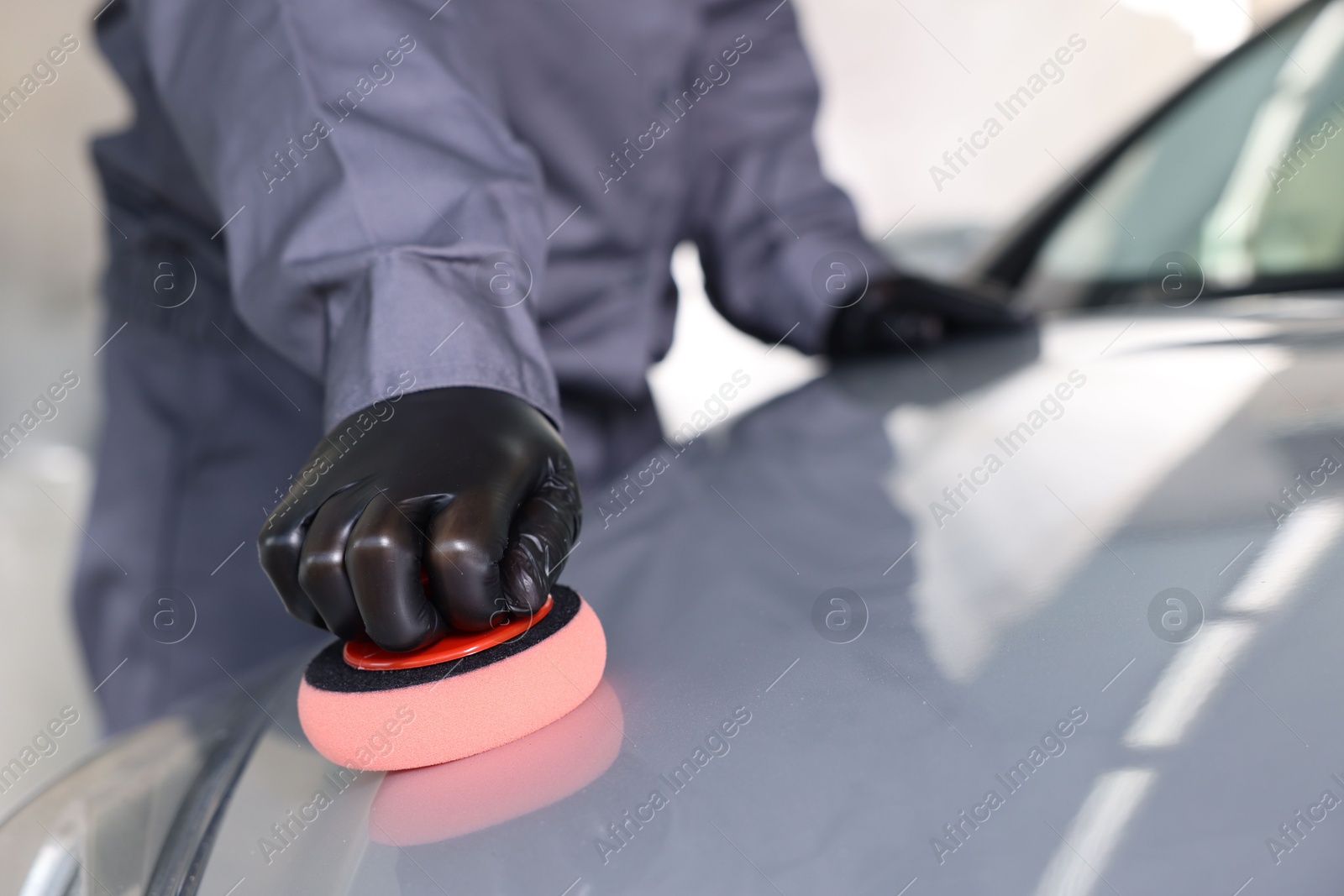 Photo of Man polishing car hood with sponge indoors, closeup