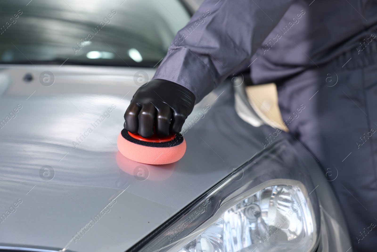 Photo of Man polishing car hood with sponge indoors, closeup