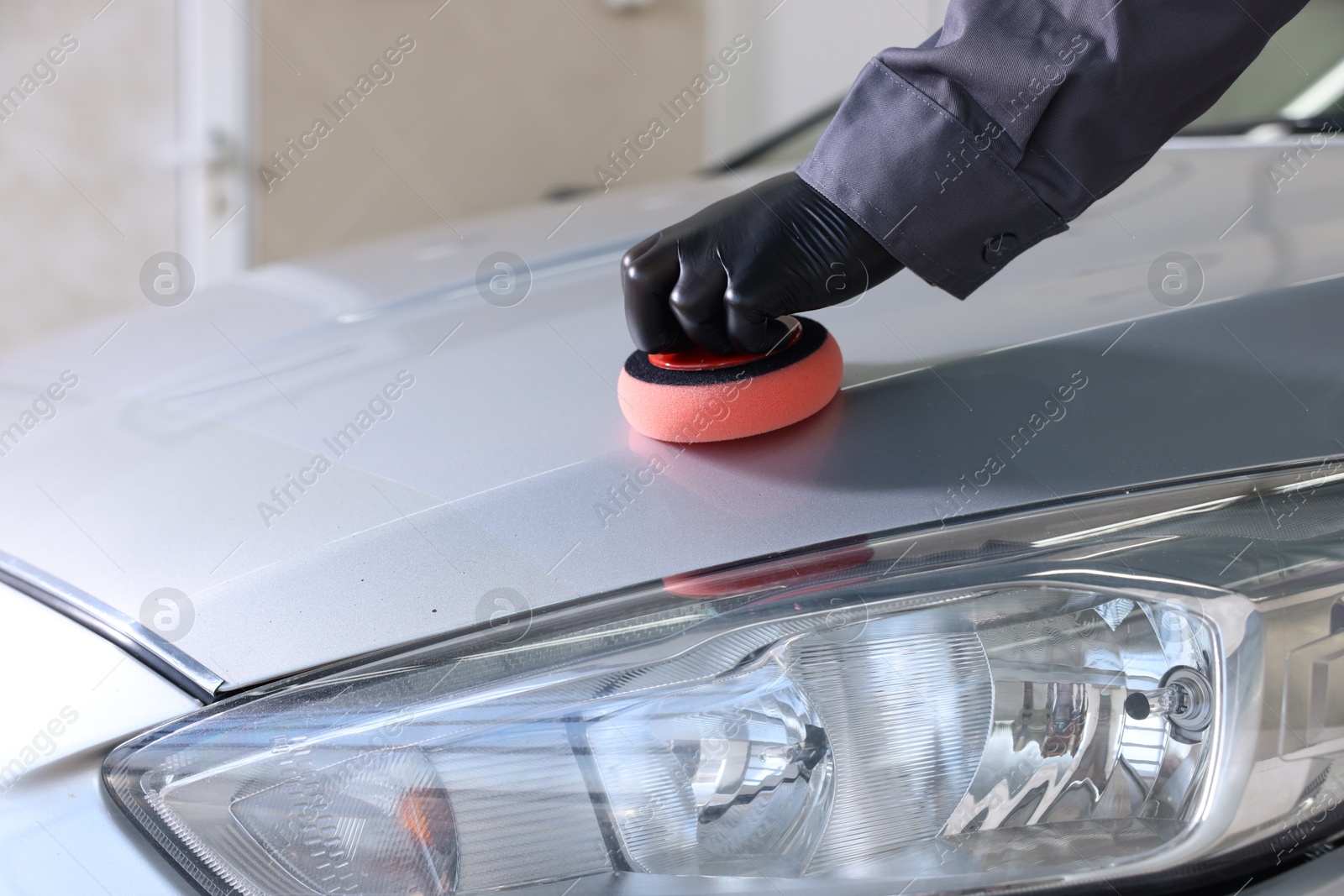 Photo of Man polishing car hood with sponge indoors, closeup