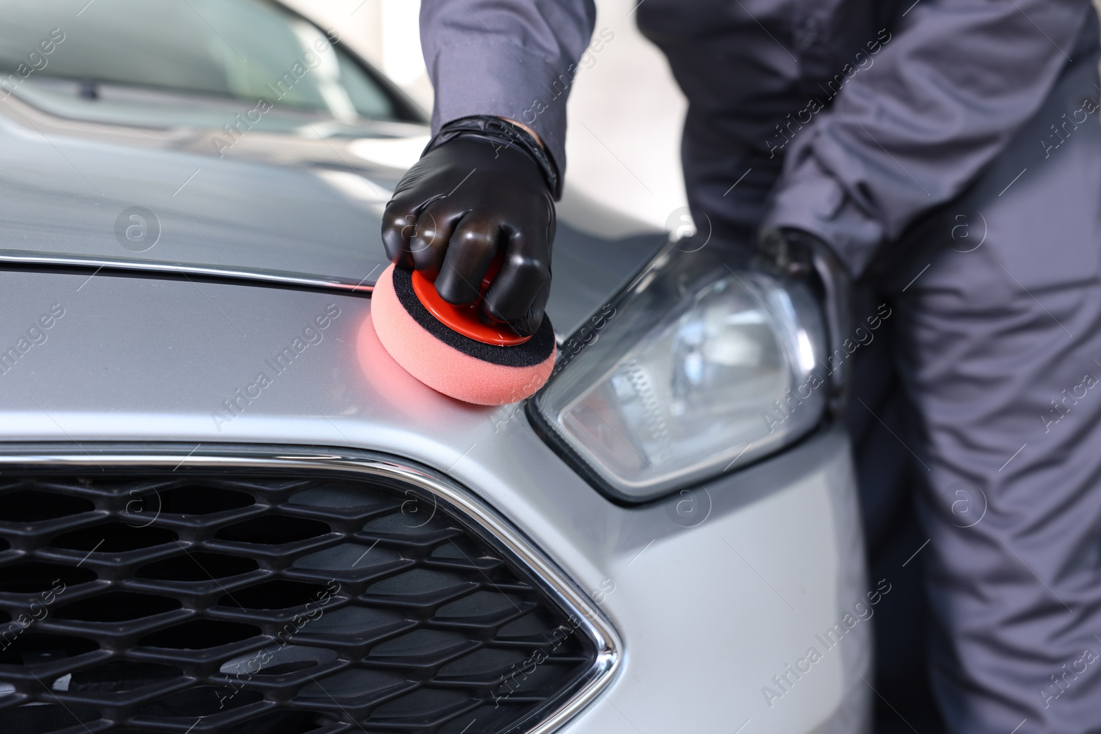 Photo of Man polishing car with sponge indoors, closeup