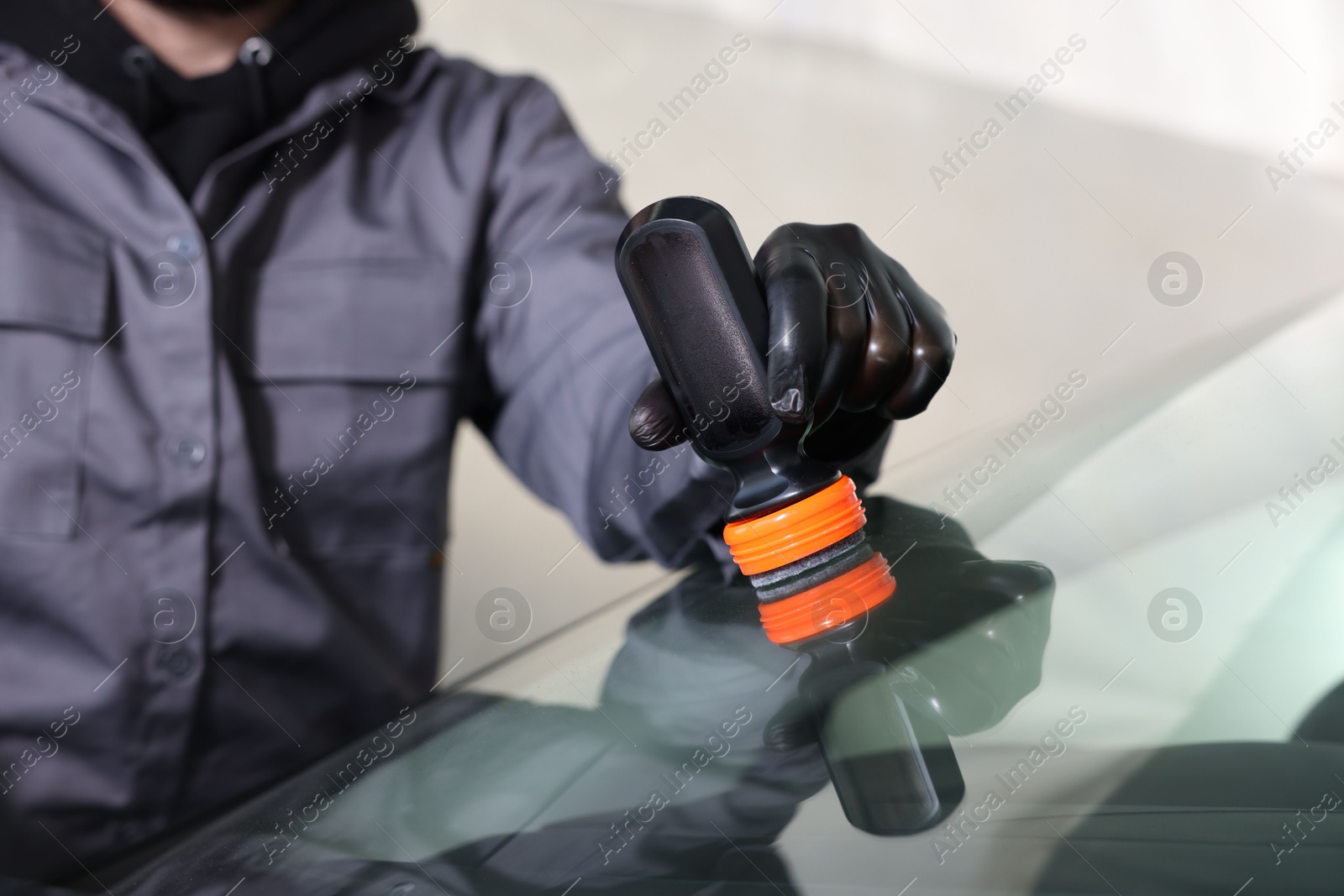 Photo of Man polishing car windshield indoors, closeup view