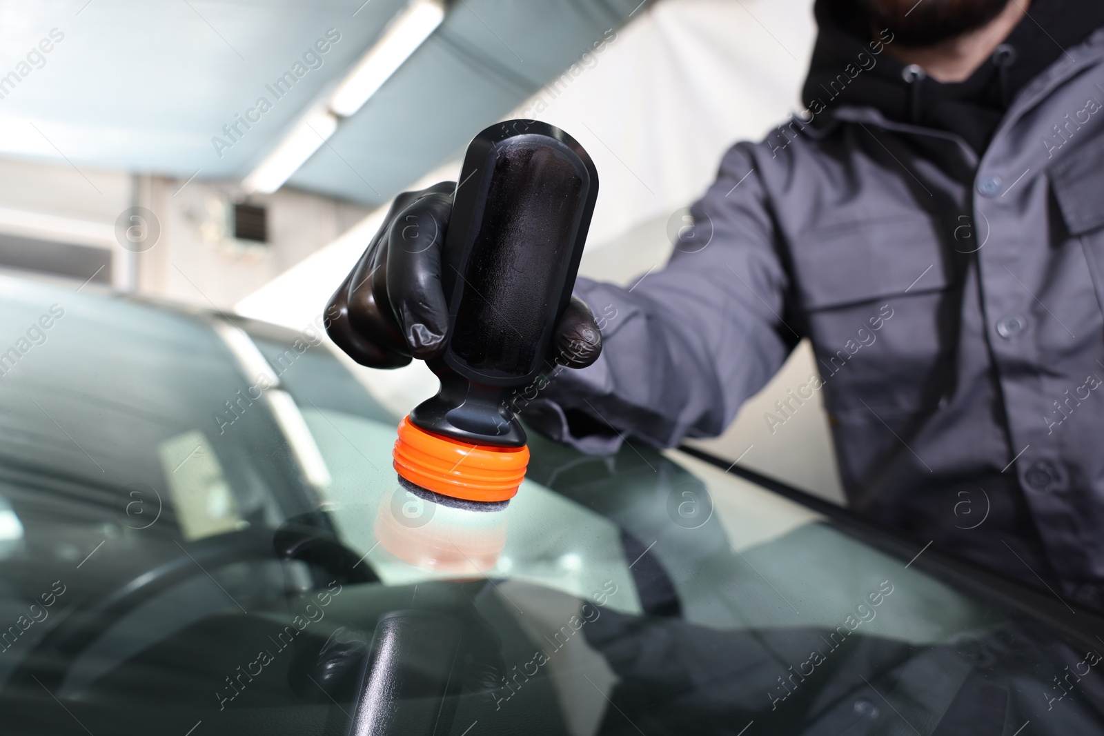 Photo of Man polishing car windshield indoors, closeup view