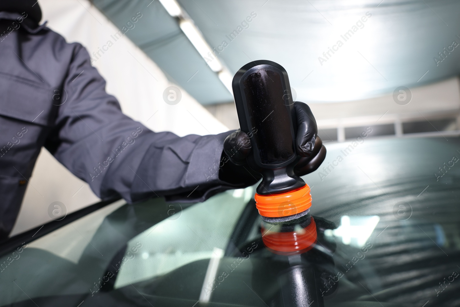 Photo of Man polishing car windshield indoors, closeup view