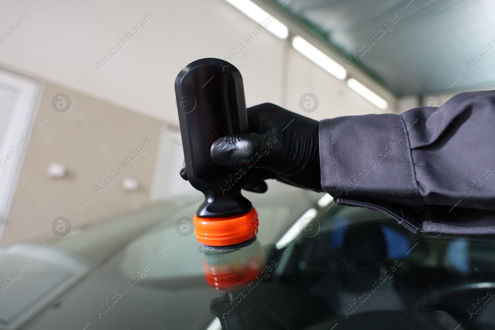 Photo of Man polishing car windshield indoors, closeup view