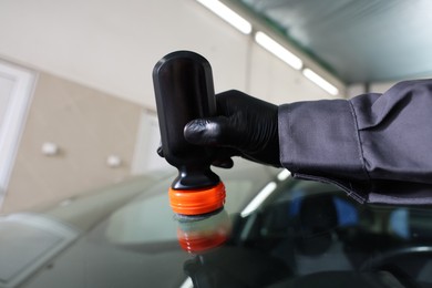 Photo of Man polishing car windshield indoors, closeup view