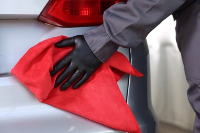 Photo of Man polishing car with red rag indoors, closeup