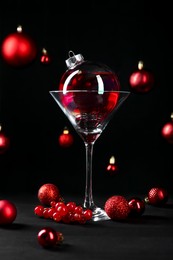 Photo of Creative presentation of Christmas cocktail in bauble and glass on black table