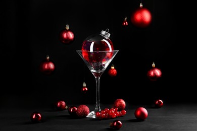 Photo of Creative presentation of Christmas cocktail in bauble and glass on black table