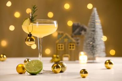 Photo of Tasty Christmas cocktail in glass and decor on white table against dark beige background with blurred lights. Space for text