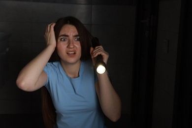 Photo of Fear of darkness. Scared young woman with flashlight indoors at night, space for text