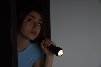 Photo of Fear of darkness. Scared young woman with flashlight indoors at night, space for text