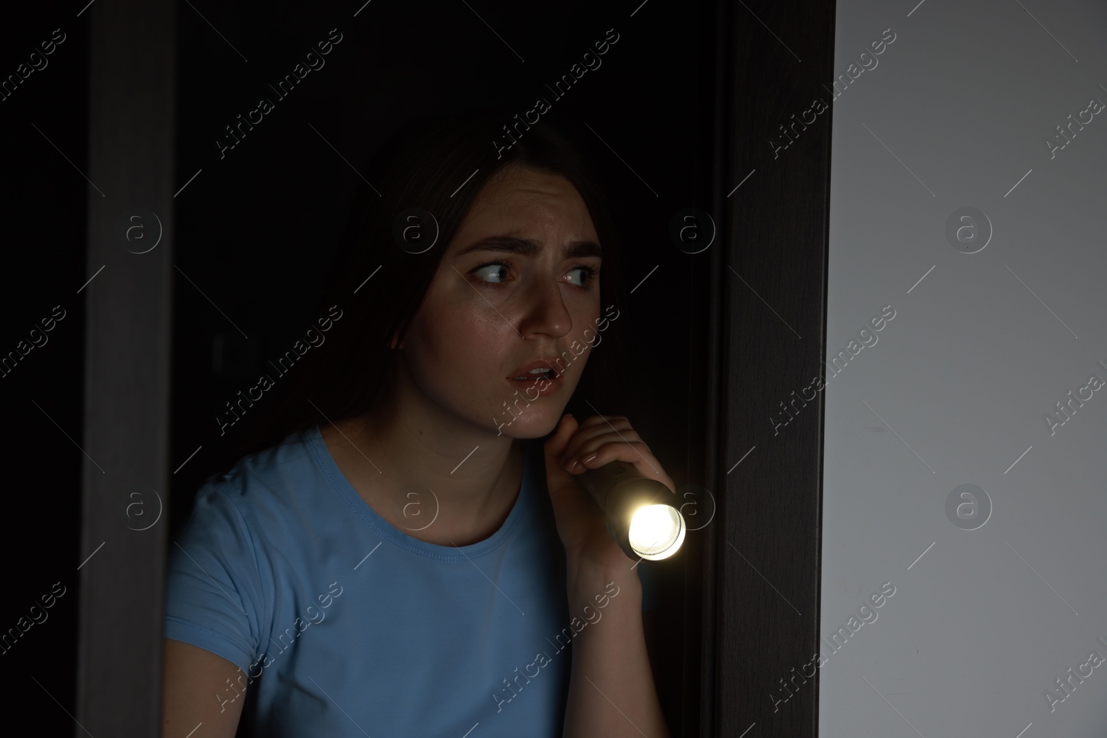 Photo of Fear of darkness. Scared young woman with flashlight indoors at night