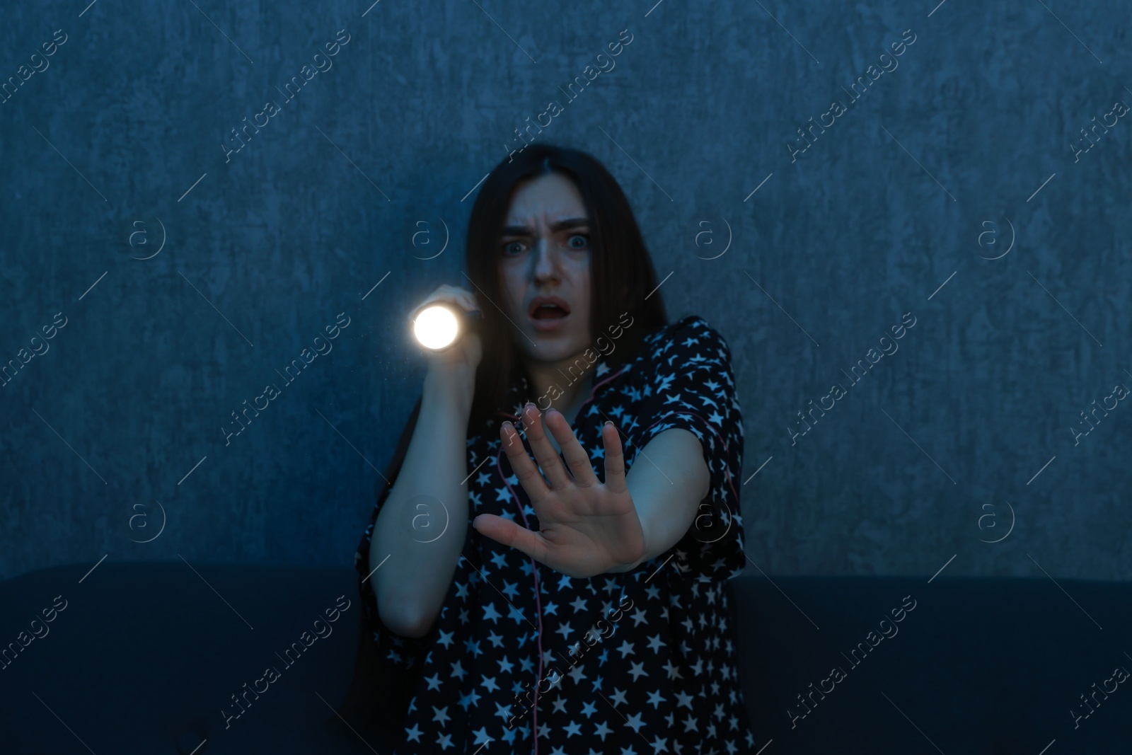 Photo of Fear of darkness. Scared young woman with flashlight on couch indoors at night