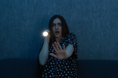 Photo of Fear of darkness. Scared young woman with flashlight on couch indoors at night