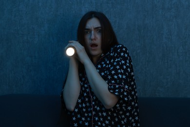 Photo of Fear of darkness. Scared young woman with flashlight on couch indoors at night