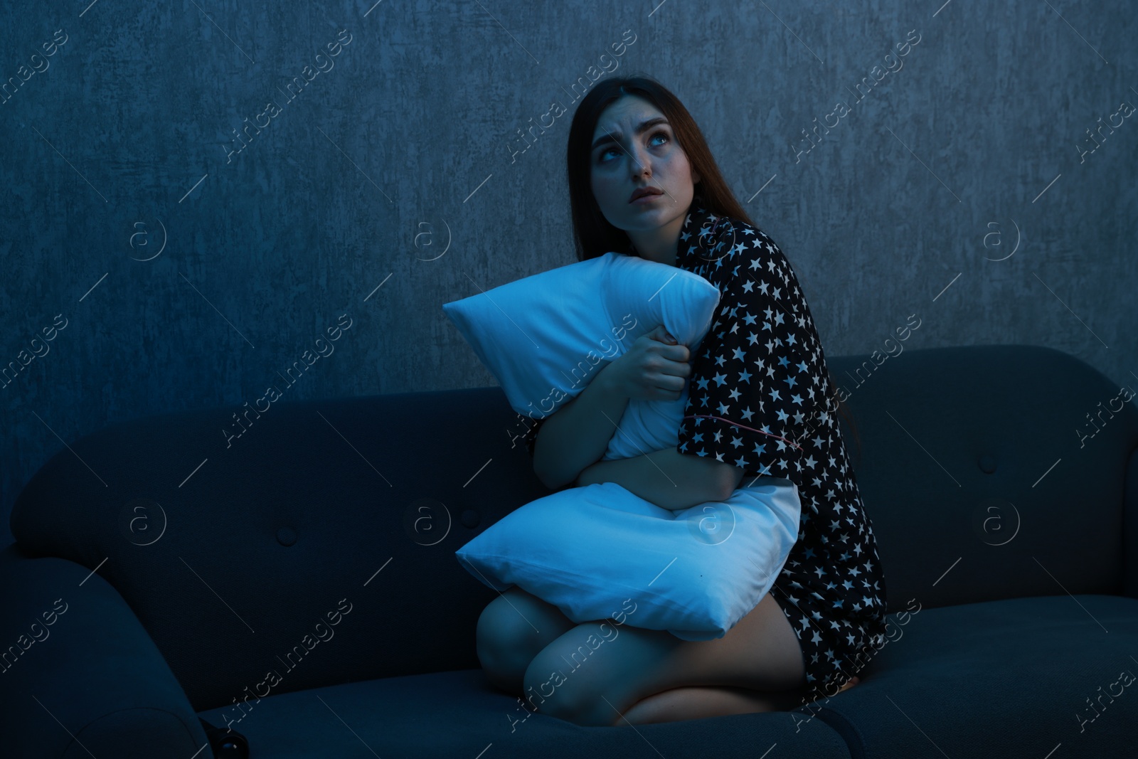 Photo of Fear of darkness. Scared young woman hugging pillow on couch indoors at night, space for text