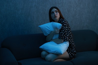 Fear of darkness. Scared young woman hugging pillow on couch indoors at night, space for text