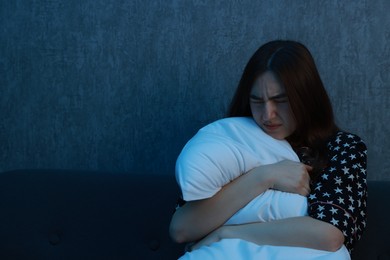 Photo of Fear of darkness. Scared young woman hugging pillow on couch indoors at night, space for text