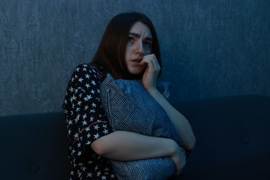 Photo of Fear of darkness. Scared young woman hugging pillow on couch indoors at night