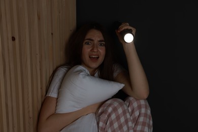 Fear of darkness. Scared young woman with flashlight hugging pillow indoors at night