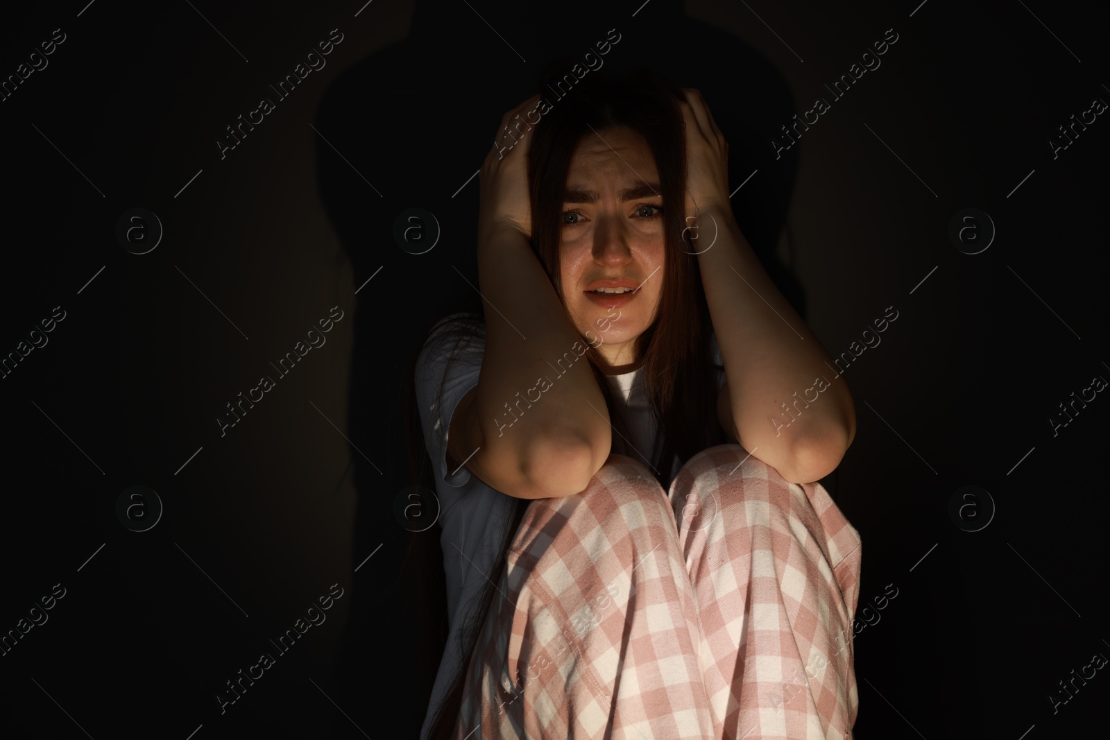 Photo of Fear of darkness. Scared young woman sitting on dark background