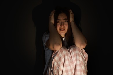 Fear of darkness. Scared young woman sitting on dark background