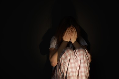 Photo of Fear of darkness. Scared young woman sitting on dark background