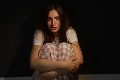 Photo of Fear of darkness. Scared young woman sitting on dark background