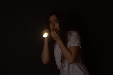 Photo of Fear of darkness. Scared young woman with flashlight indoors at night