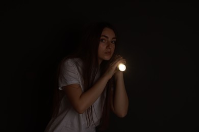 Photo of Fear of darkness. Scared young woman with flashlight indoors at night