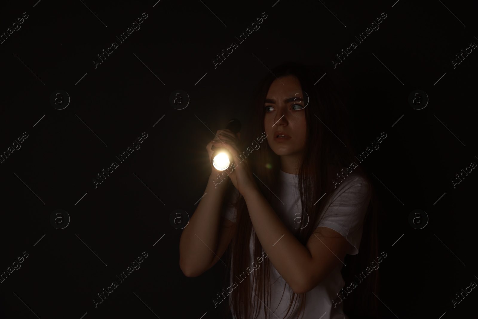 Photo of Fear of darkness. Scared young woman with flashlight indoors at night