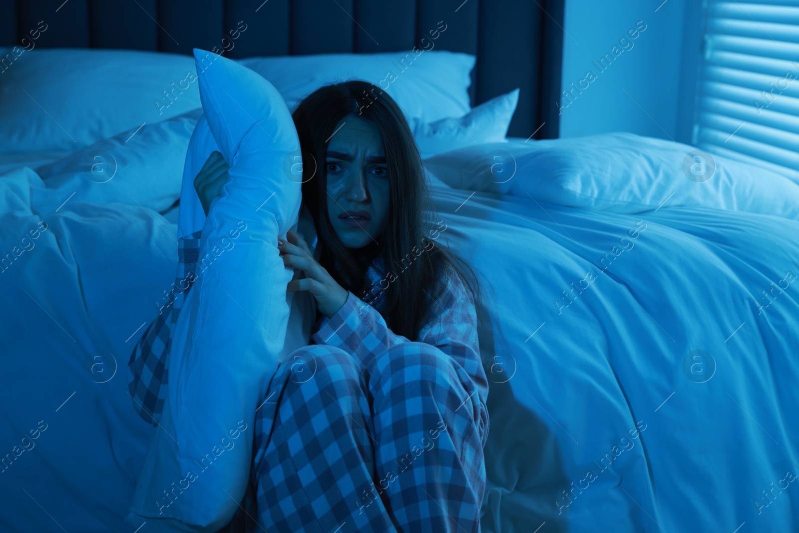 Photo of Fear of darkness. Scared young woman hugging pillow in bedroom at night