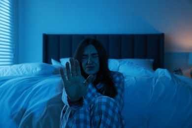 Fear of darkness. Scared young woman showing stop gesture in bedroom at night