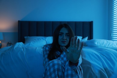 Photo of Fear of darkness. Scared young woman showing stop gesture in bedroom at night