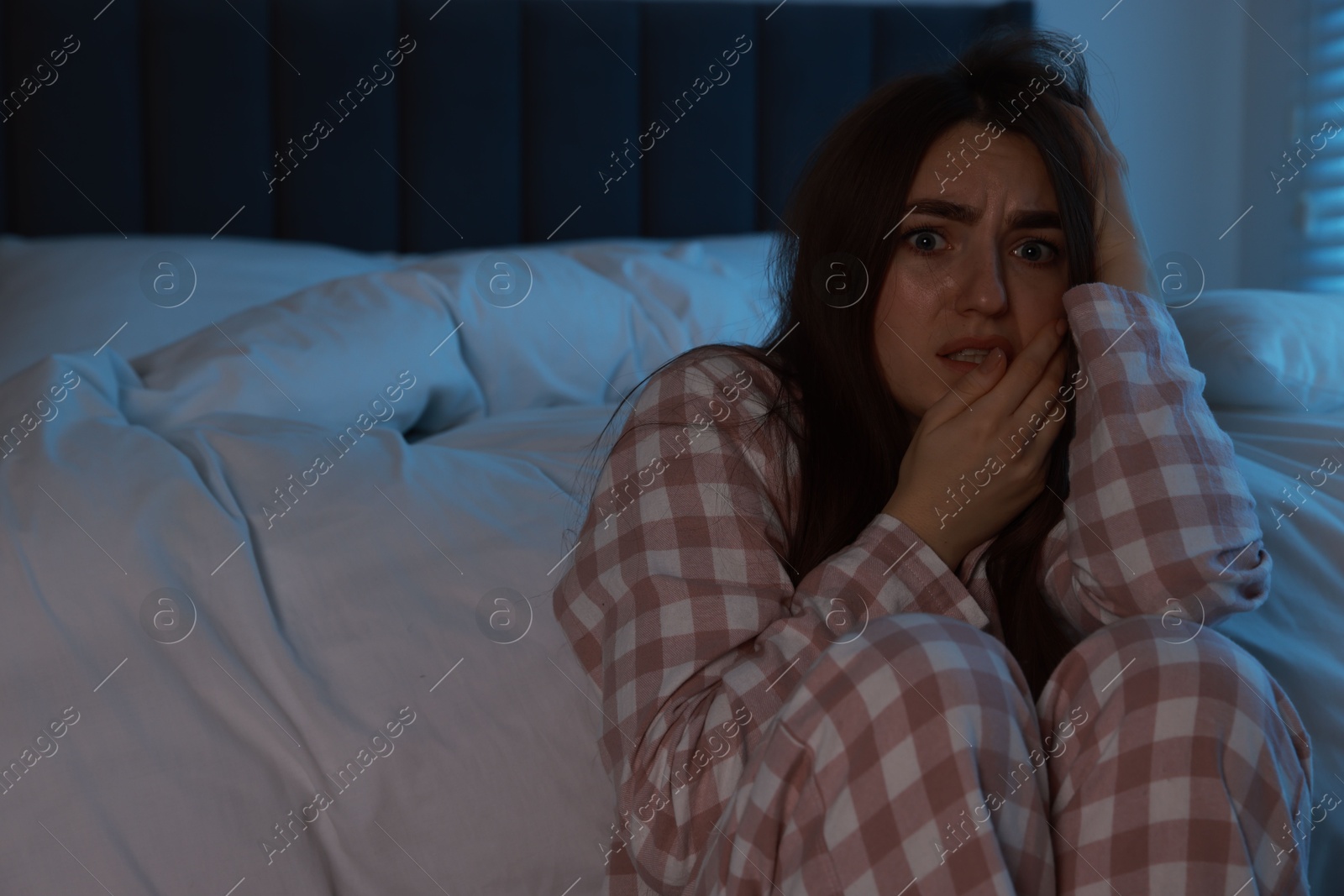 Photo of Fear of darkness. Scared young woman in bedroom at night, space for text