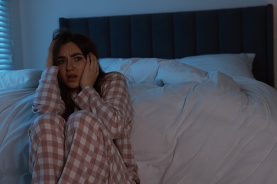 Photo of Fear of darkness. Scared young woman in bedroom at night, space for text