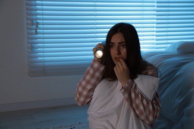 Photo of Fear of darkness. Scared young woman with flashlight hugging pillow in bedroom at night, space for text