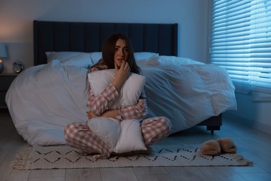 Fear of darkness. Scared young woman hugging pillow in bedroom at night