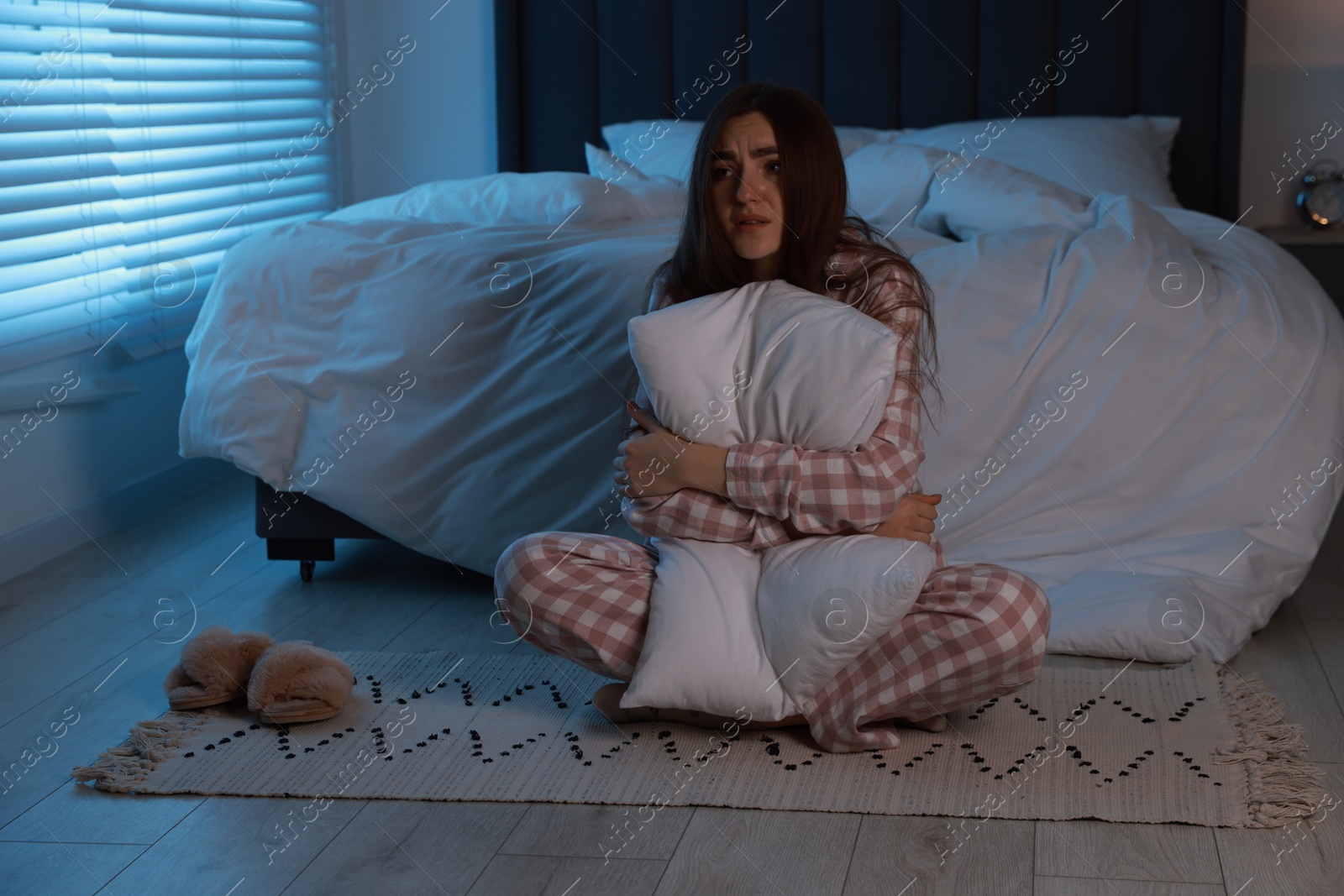 Photo of Fear of darkness. Scared young woman hugging pillow in bedroom at night