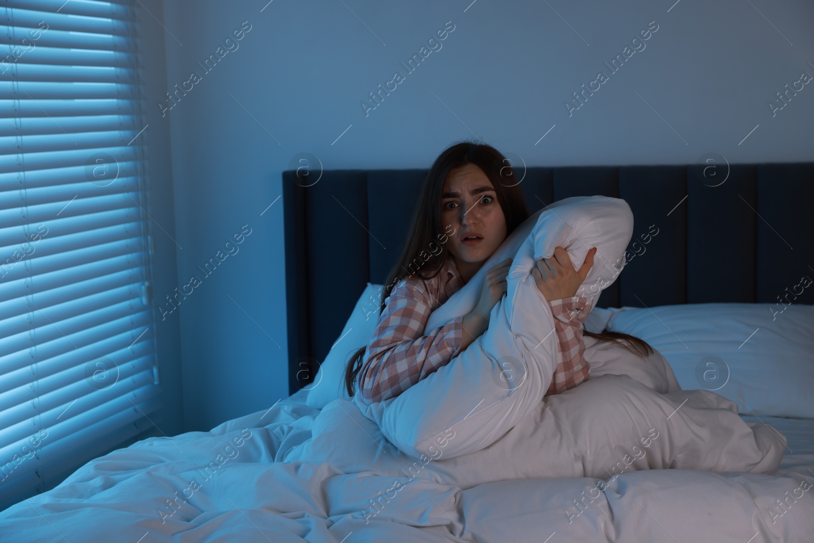 Photo of Fear of darkness. Scared young woman lying on bed in room at night