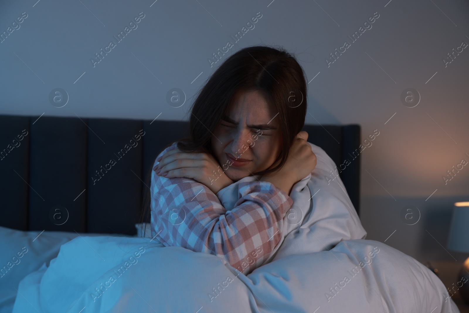 Photo of Fear of darkness. Scared young woman lying on bed in room at night