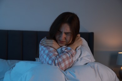 Photo of Fear of darkness. Scared young woman lying on bed in room at night