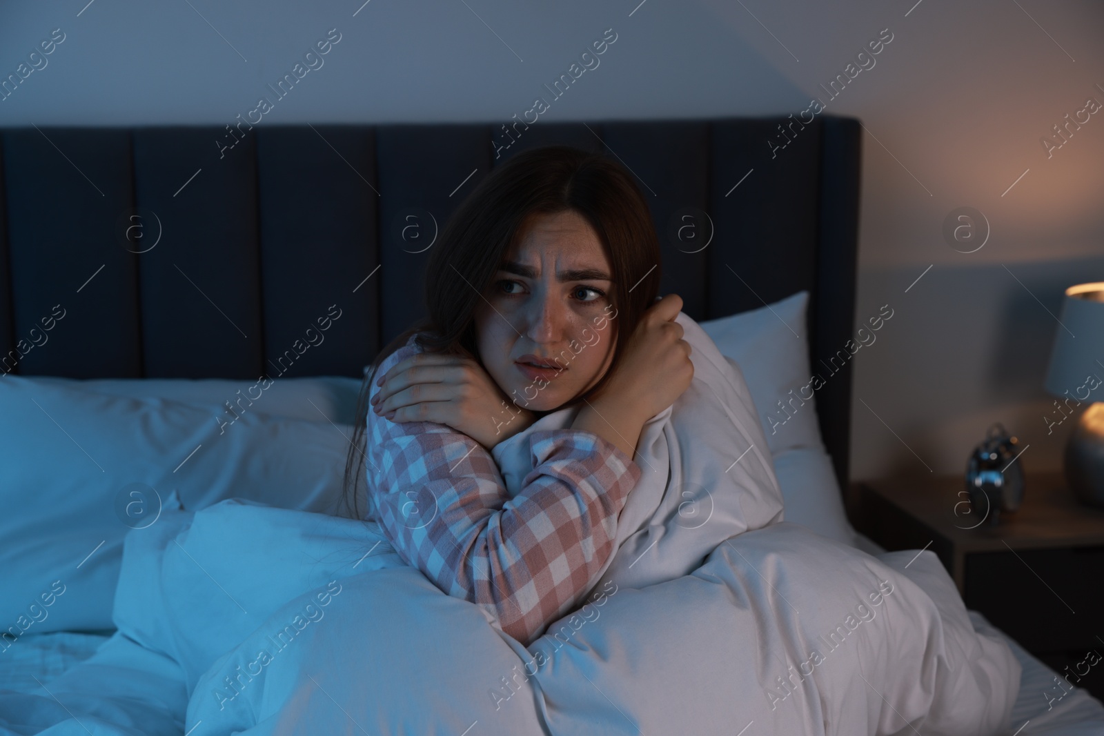 Photo of Fear of darkness. Scared young woman lying on bed in room at night