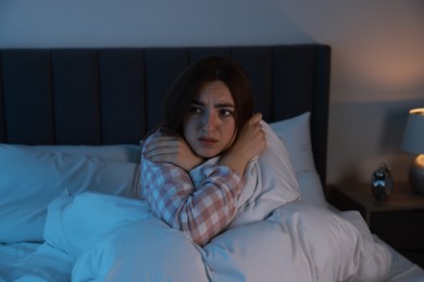 Photo of Fear of darkness. Scared young woman lying on bed in room at night