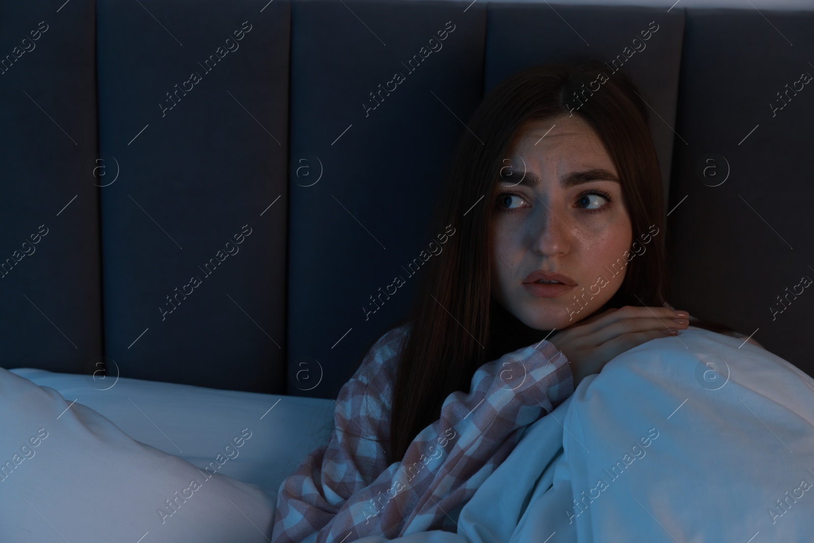 Photo of Fear of darkness. Scared young woman lying on bed in room at night, space for text