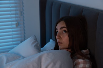 Photo of Fear of darkness. Scared young woman lying on bed in room at night, space for text