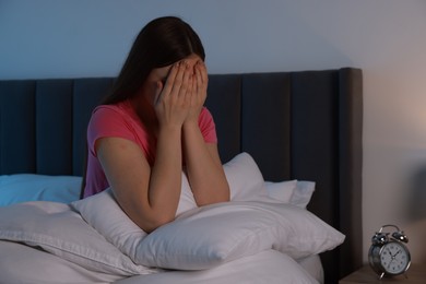 Photo of Fear of darkness. Scared young woman on bed and hiding her face in room at night