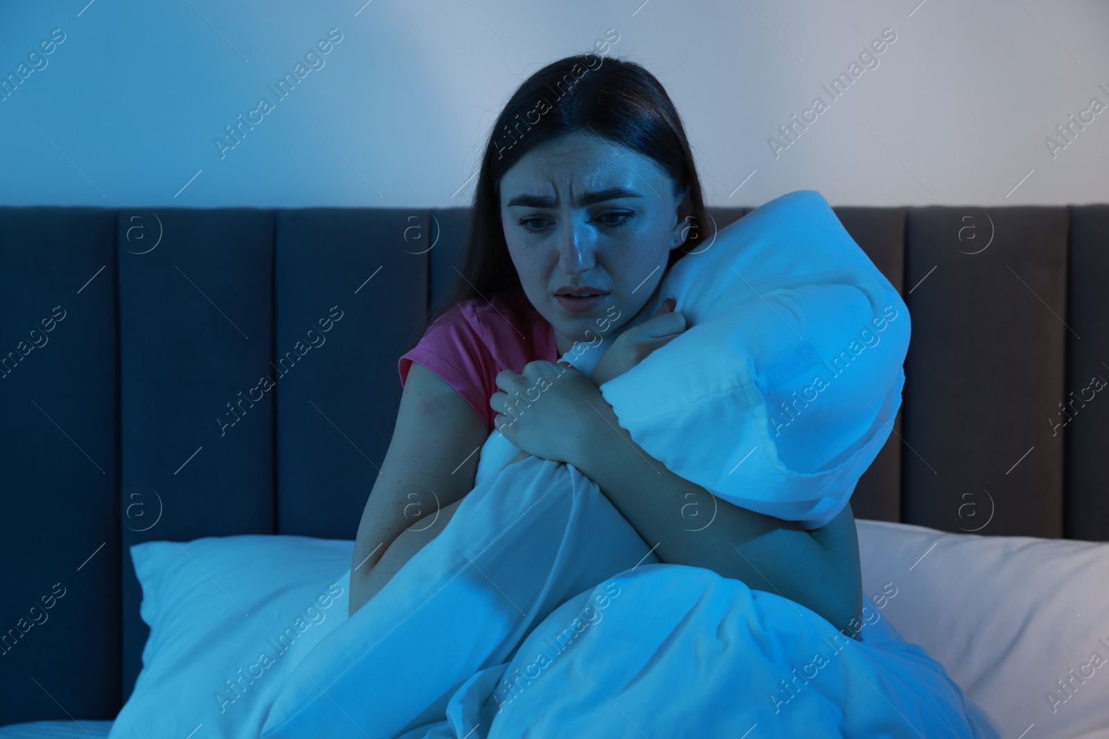 Photo of Fear of darkness. Scared young woman on bed in room at night