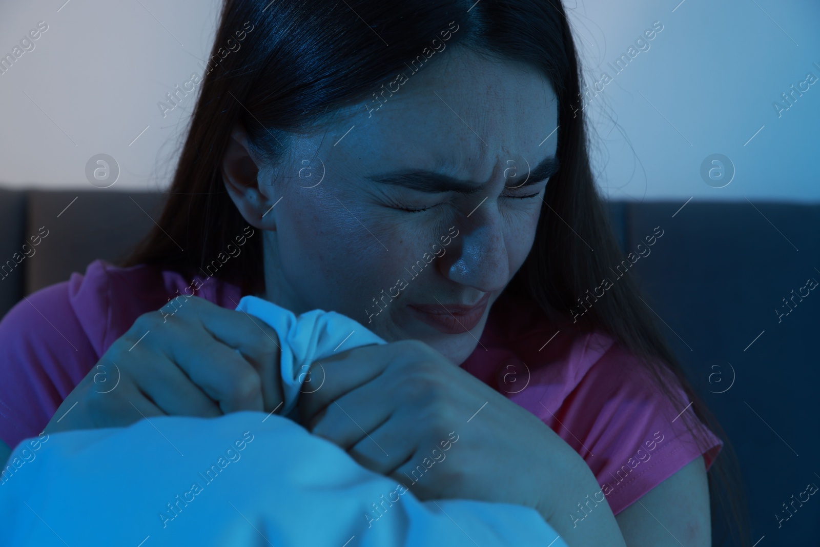 Photo of Fear of darkness. Scared young woman on bed in room at night